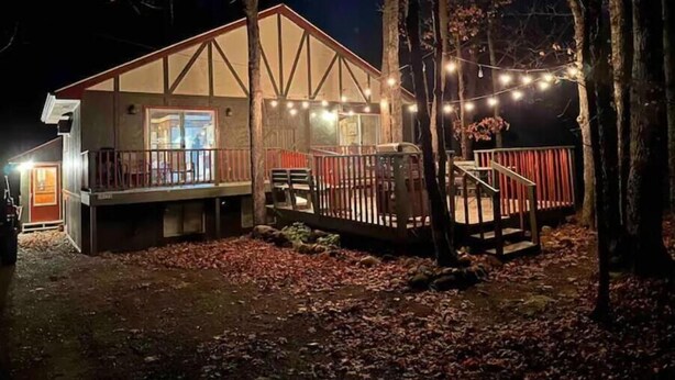 A cabin with a deck, surrounded by trees and lit by string lights. - Cozy 3BR Ski-Chalet Style Retreat w/ Sauna + Fireplace— Outdoor Adventure Base (Bessemer)