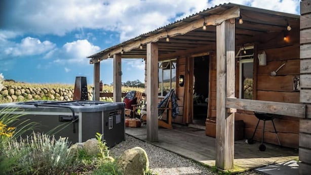 Ein rustikales Blockhaus mit Holzfassade, einer Veranda und einer Badewanne im Vordergrund.