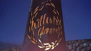 Eine hohe, dunkel gefärbte Säule mit dem Schriftzug "Willentree Glamping" und einem dekorativen Kranz.