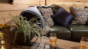 Ein gemütliches Zimmer mit einem Ledersofa, gemusterten Kissen, einer Topfpflanze und zwei Gläser bernsteinfarbener Flüssigkeit auf einem Holztisch.