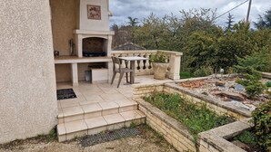 Un patio con una parrilla, mobiliario exterior y un pequeño jardín.