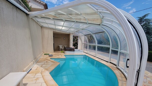 A swimming pool with a glass enclosure, stone tiles, and a bench. - Grande Maison Avec Piscine Chauffée et spa (Lablachère)