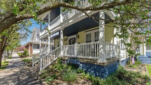 A two-story house with a porch, white railings, and a small garden area.