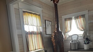 A dining area with a table and chairs, a giraffe sculpture, and a window with curtains.