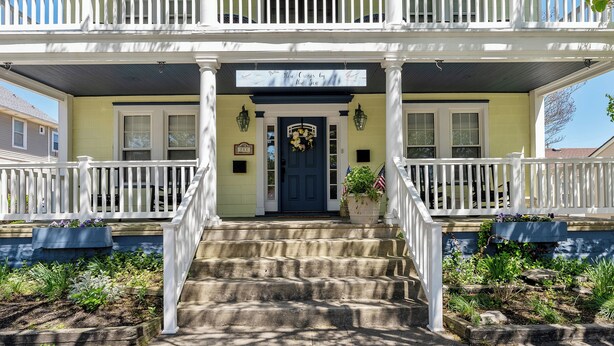 A two-story house with a front porch, a blue door, and a sign above the door.