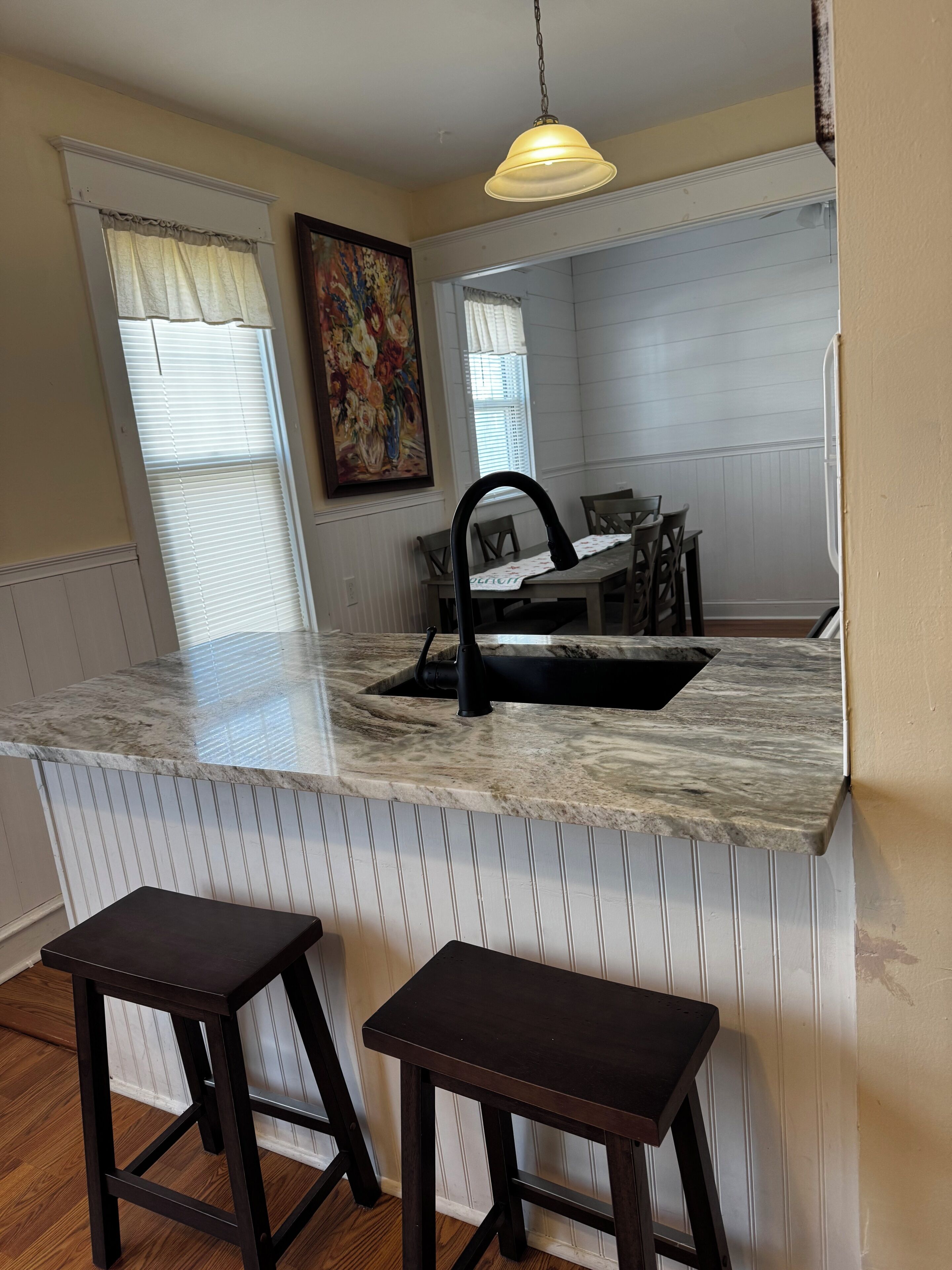 A kitchen with a marble countertop, a black faucet, two wooden stools, and a hanging pendant light.