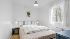 Ein Schlafzimmer mit einem Bett, Nachttischen, einer Hängelampe, einem Fenster mit Vorhängen und einem gerahmten Bild an der Wand.
