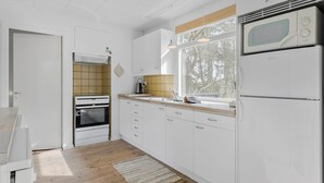 Eine moderne Küche mit weißen Schränken, einem eingebauten Ofen, einer Mikrowelle und einem Fenster, das natürliches Licht hereinlässt.