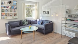 Ein modernes Wohnzimmer mit einem grauen Sofa, einem runden Couchtisch und einer Bücherwand voller Bücher.