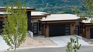 A modern two-story house with a garage, surrounded by a landscaped driveway and a view of mountains.