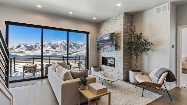 A modern living room with a large window overlooking snow-capped mountains, a fireplace, and a cozy seating area.