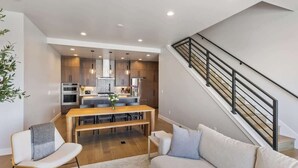 A modern kitchen with a dining area, a staircase, and a living room with a sofa and a chair.