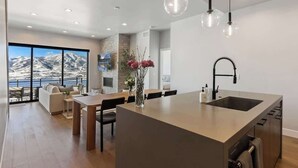 A modern kitchen with a large island, a dining area with a view, and a living space with a sofa and a coffee table.