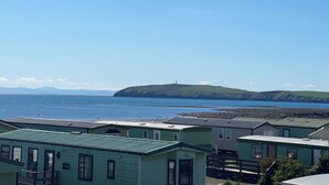 A coastal area with several small, light-colored cabins with green roofs, arranged in a row. - 3 Bedroom Lodge, Close to Beach, Stunning Views, includes hot tub (Drummore)