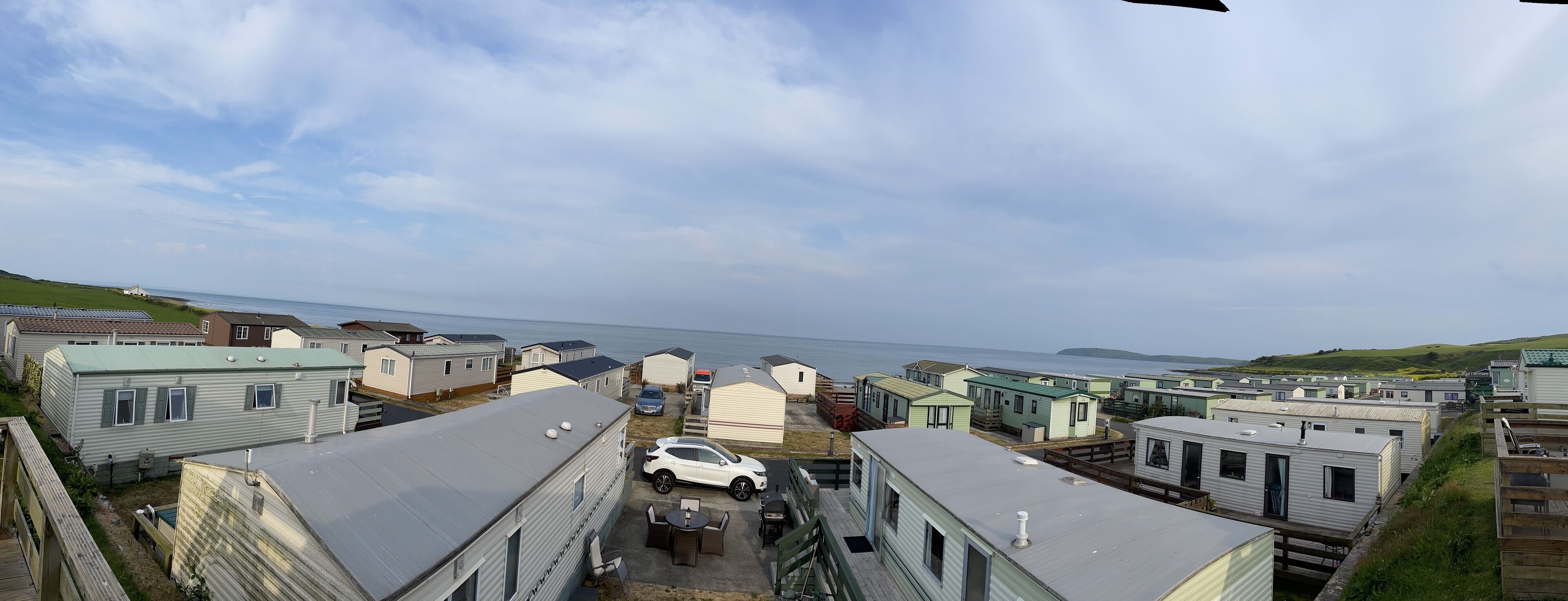 A caravan park with multiple mobile homes, a white car parked in front, and a view of the sea in the background.
