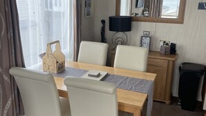 A compact, well-lit room with a dining table, chairs, a small desk, and a trash bin. - 3 Bedroom Lodge, Close to Beach, Stunning Views, includes hot tub (Drummore)