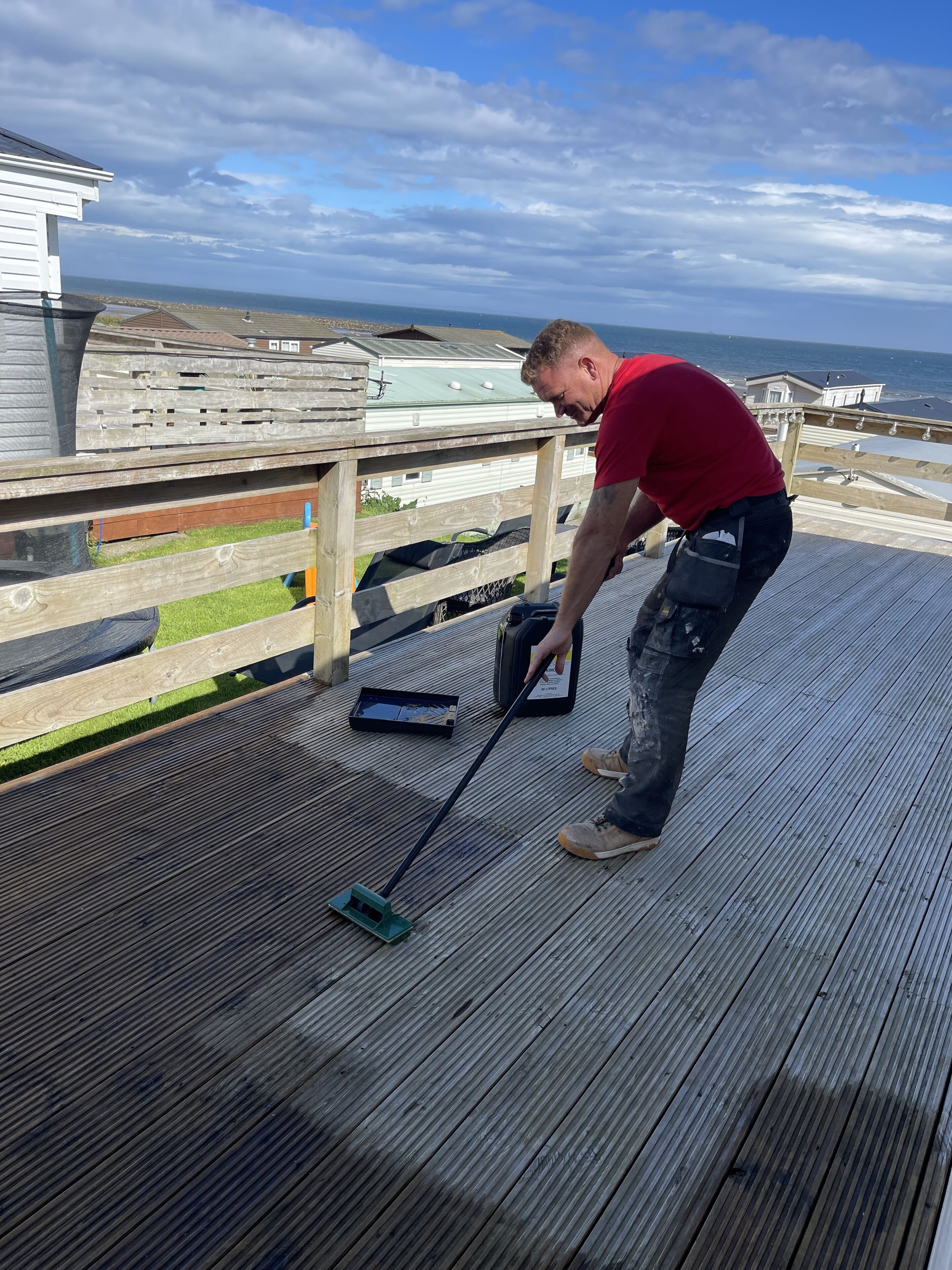 Una persona barriendo y recogiendo hojas en una terraza de madera.