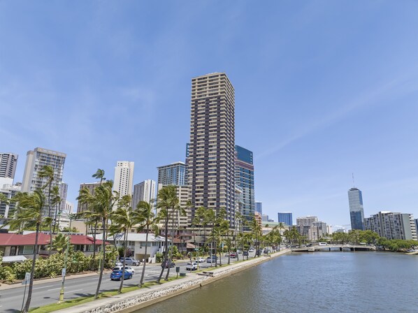 A high-rise building with a modern design, surrounded by palm trees and a river.