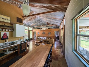 A rustic kitchen with a long wooden table, a dining area with a sofa, and a large window.