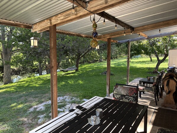 A covered patio area with a wooden table, chairs, and a hammock.