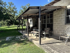A covered patio area with outdoor furniture, a stone building, and a grassy yard.