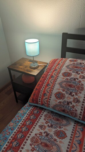 A bed with a patterned blanket, a bedside table with a lamp, and a chair. - Pale Blue Dot (Platteville)