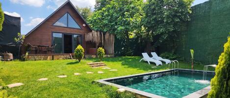 Una casa con piscina, un patio con sillas y un jardín.