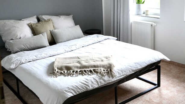 Une chambre à coucher avec un lit, une fenêtre avec des rideaux, un radiateur et un ventilateur de plafond.