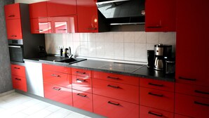 Une cuisine moderne avec des meubles de couleur rouge, une hotte de cuisinière en acier inoxydable et une machine à café posée sur le plan de travail.