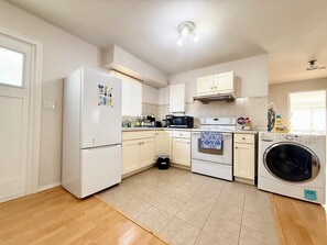 A compact kitchen with white appliances, a tiled floor, and a window with blinds.