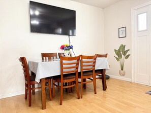 A dining area with a table set for four, wooden chairs, a vase with flowers, and a flat-screen TV mounted on the wall.