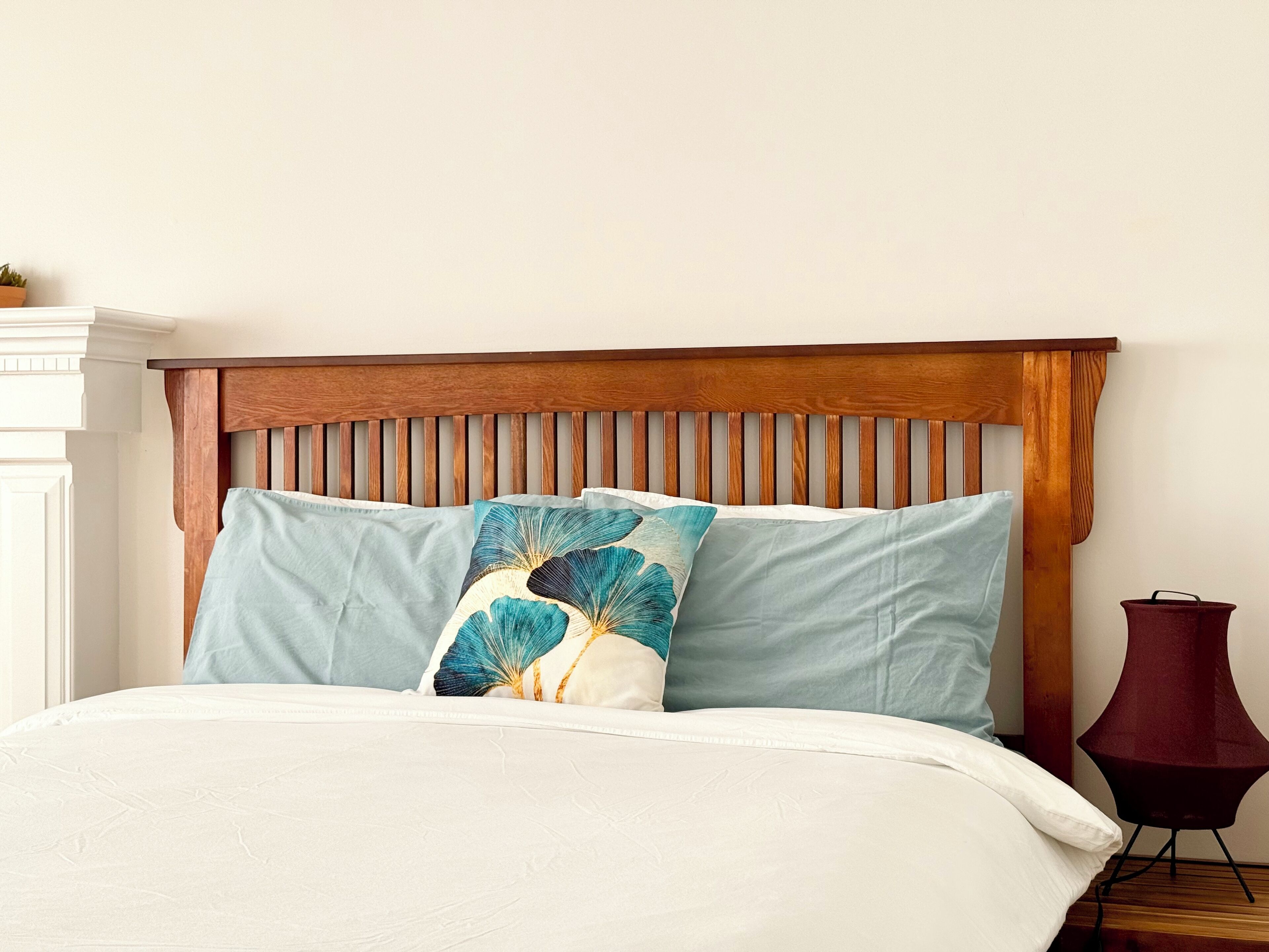 Un lit avec une tête de lit en bois, des oreillers bleu clair et blancs, et une couvre-lit blanche.