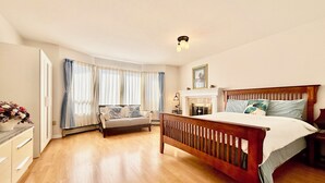 Une chambre spacieuse avec un grand lit, un canapé, une cheminée et une vue sur l’ext érieur grâce à de grandes fenêtres.