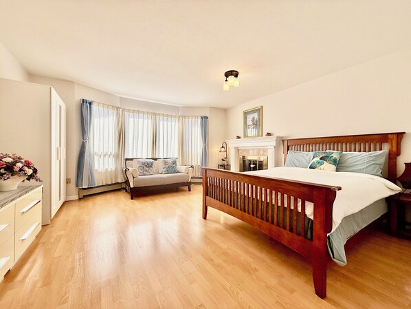 A spacious bedroom with a large bed, a sofa, a fireplace, and a view of the outdoors through large windows.