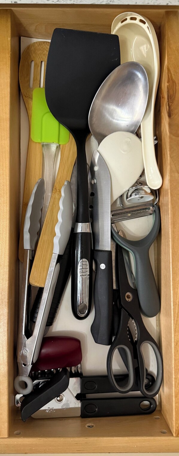 A drawer containing various kitchen utensils including a knife, spatula, spoon, and scissors.