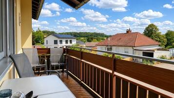 Un balcon avec une table et des chaises, une sphère de verre décorative, et une vue sur des maisons et des arbres.