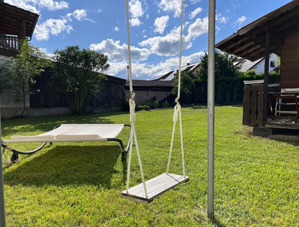 A backyard with a swing set, a lounge chair, and a wooden pergola.