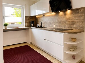 A modern kitchen with white cabinets, a wooden backsplash, a built-in TV, and a red rug.