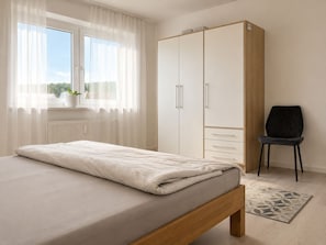 A bedroom with a bed, a wardrobe, a chair, and a window with curtains.