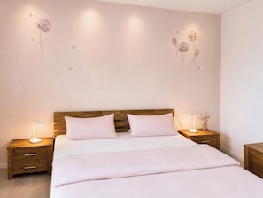 Un dormitorio con cabecera de madera, dos mesitas de noche, una cama con ropa blanca y un cuadro de flores en la pared.