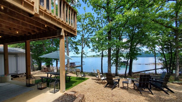 Un patio techado con mobiliario exterior, vistas a un lago y una terraza de madera con vistas al agua.