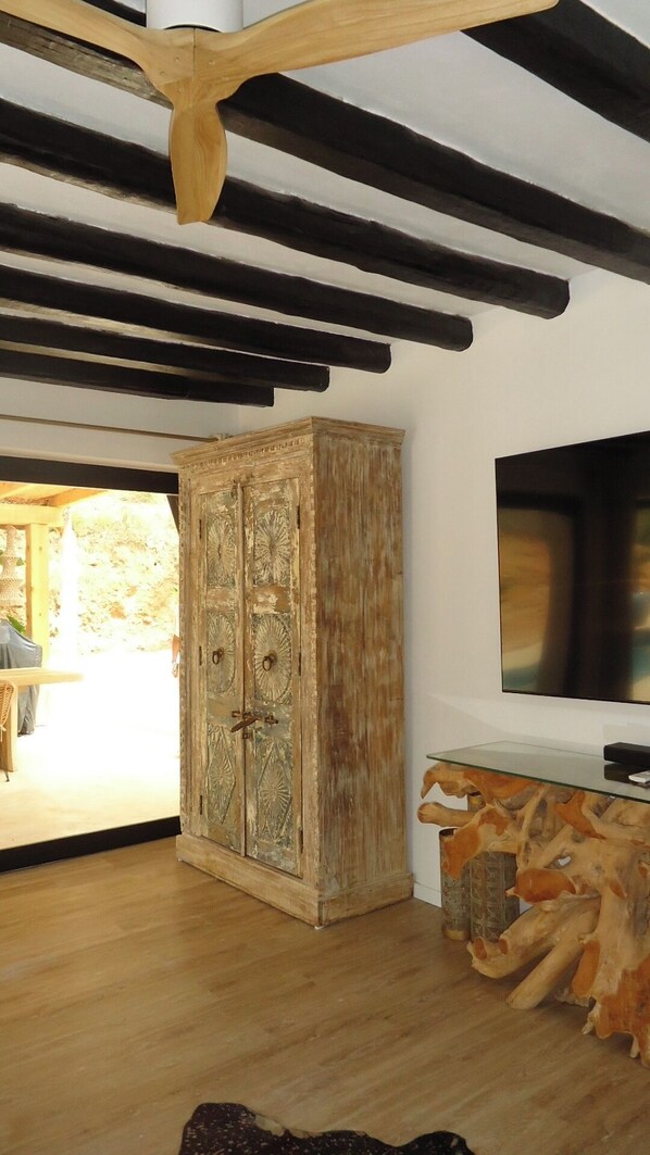 A room with exposed wooden beams, a rustic wooden cabinet with intricate carvings, and a glass-top coffee table with a natural wood base.