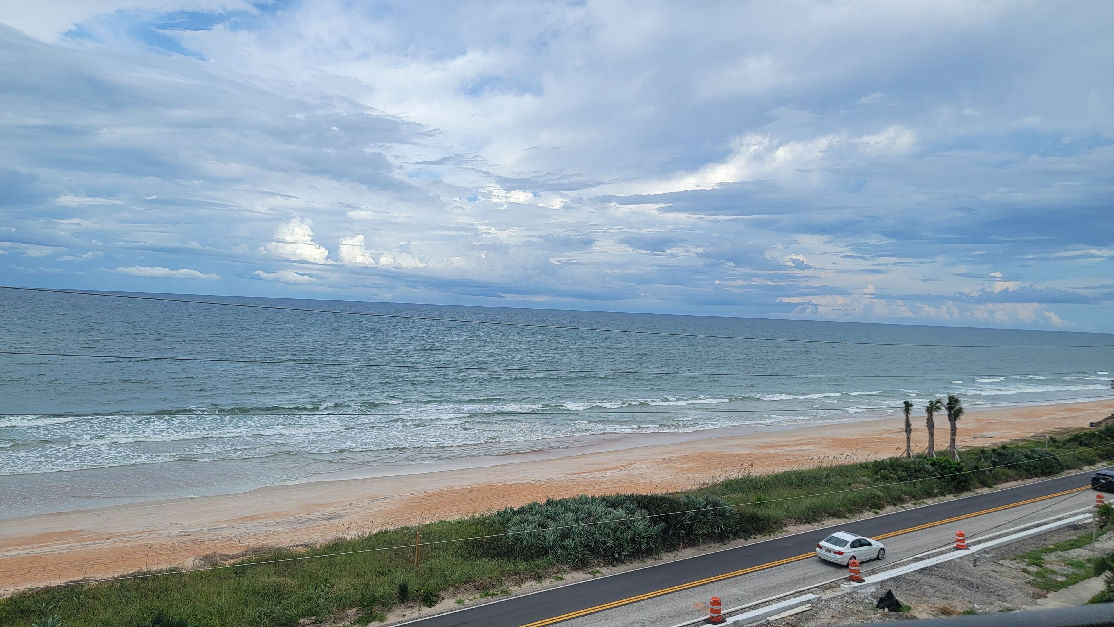 Une route côtière bordée d’une plage, avec l’océan et un ciel nuageux.