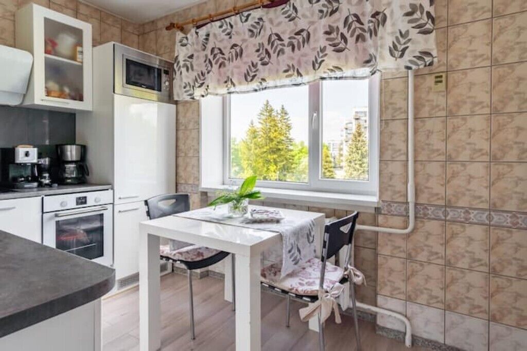 A kitchen with a dining table, chairs, a microwave, a coffee maker, and a window with a view of trees.