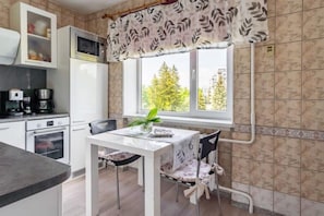 Une cuisine équipée d’une table à manger, de chaises, d’un four à micro-ondes, d’une machine à café et d’une fenêtre donnant sur la verdure.