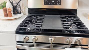 Una cocina con estufa, horno de acero inoxidable y encimera blanca.