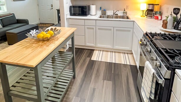 A modern kitchen with white cabinets, a black microwave, a stove, and a wooden table with a yellow flower arrangement. - Private Dallas/Bishop Arts Retreat  (Dallas)