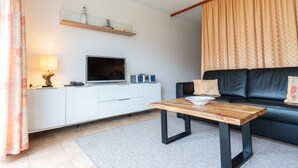 Una sala de estar moderna con una televisión de pantalla plana, una mesa de centro de madera, un sofá de cuero negro y un armario blanco.