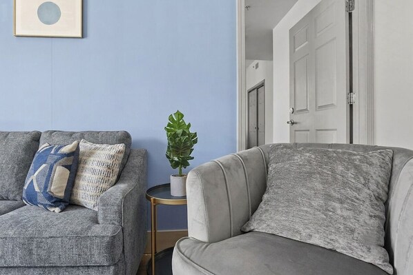 A living room with two grey sofas, one with patterned cushions, and a small side table with a plant.