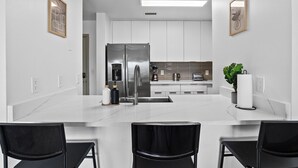 A modern kitchen with white cabinets, stainless steel appliances, and a marble countertop.